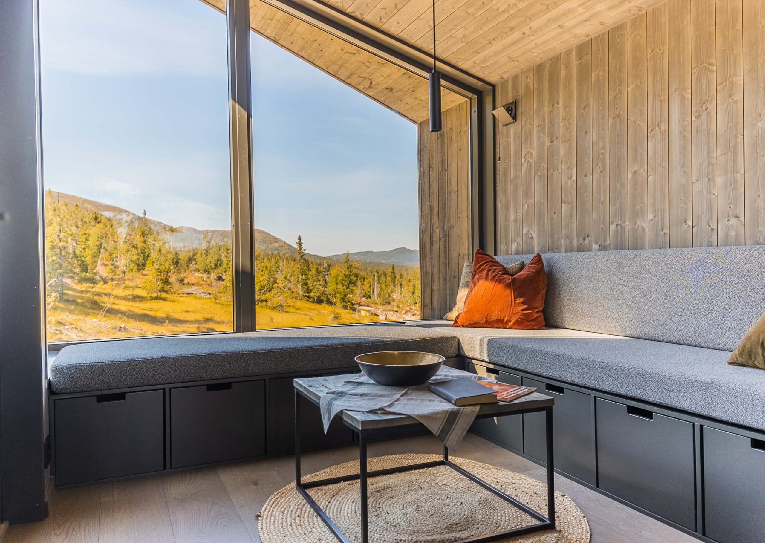 Foto. Interiør stue med plassbygd hjørnesofa. Store vinduer med utsikt til fjellandskap i høstfarger.