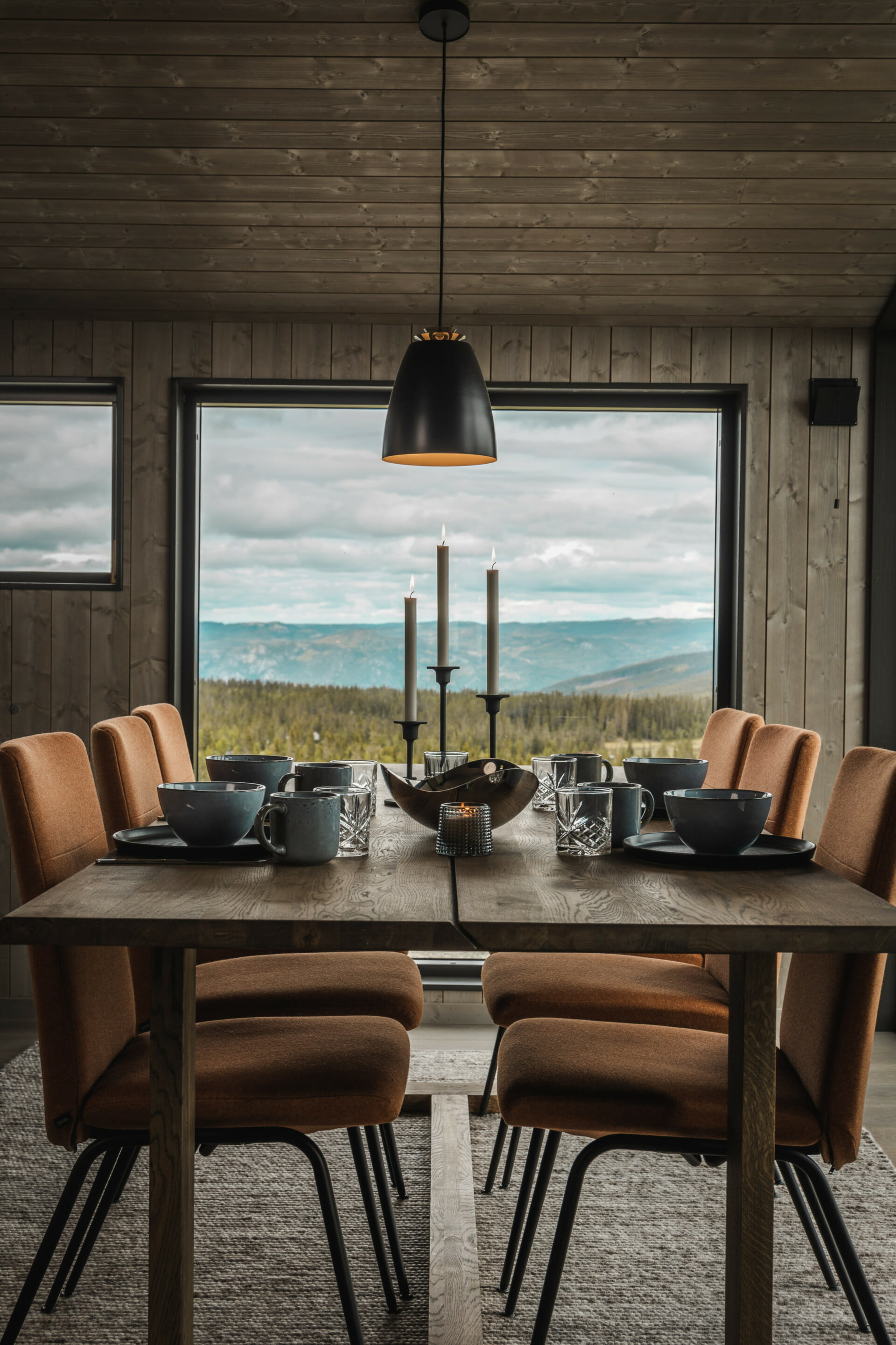 Foto. Dekket spisebord i hytte med utsikt til fjell utenfor.