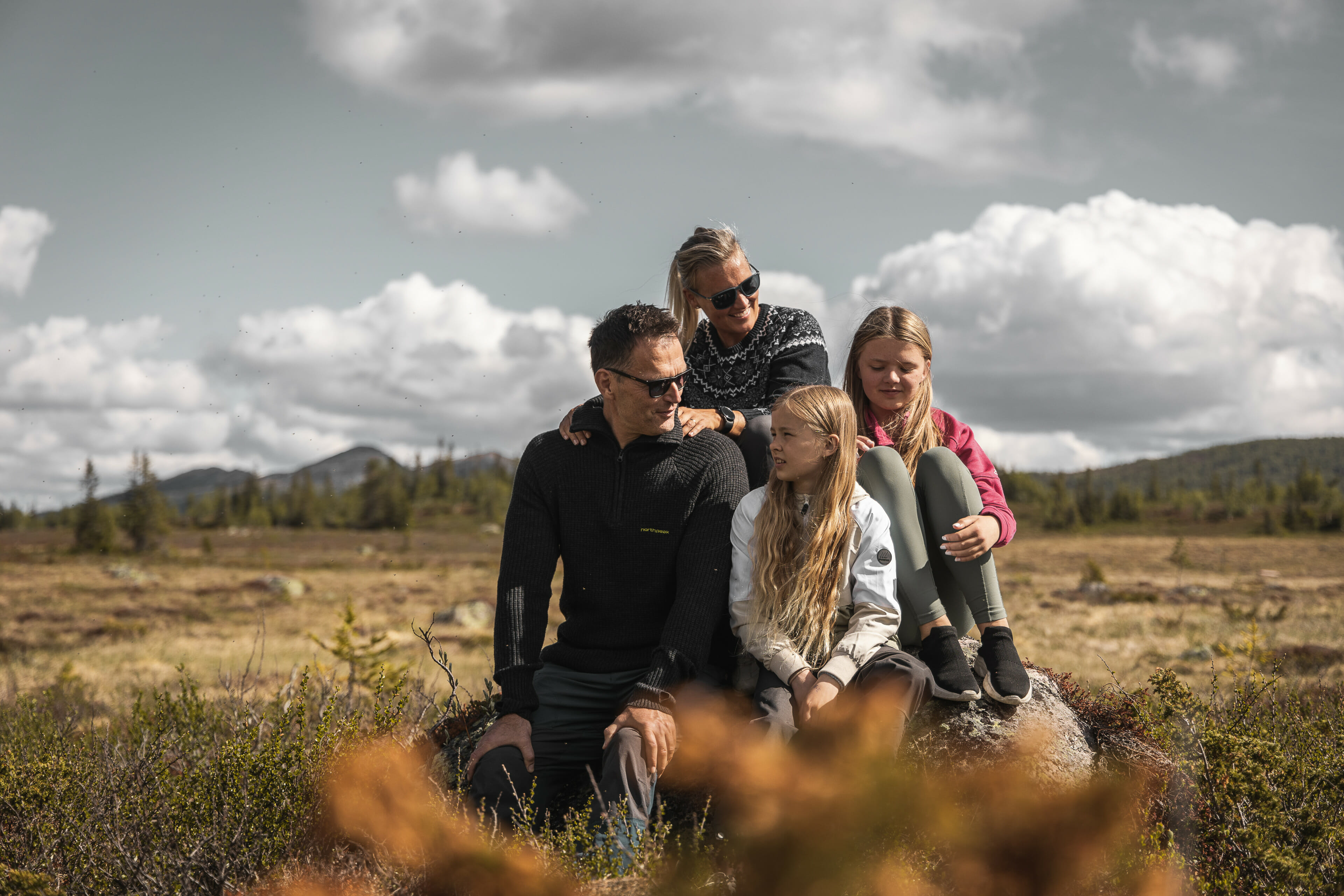 Foto. Fjellandskap. Familie på fire sitter på en stein.