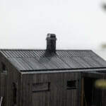 LY Hytta med brun trekledning på vegger og tak. Solcelleanlegg på taket. Tåke i bakgrunnen. Foto.